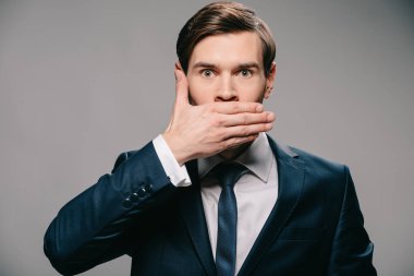 handsome businessman covering mouth with hand on grey background clipart