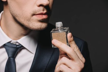 cropped view of man smelling perfume isolated on black clipart