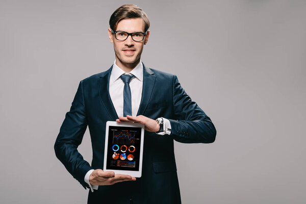 cheerful businessman holding digital tablet with charts and graphs on screen isolated on grey 