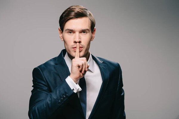 handsome businessman putting finger on lips on grey background