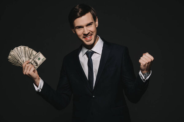 cheerful businessman holding dollar banknoted in hands isolated on black