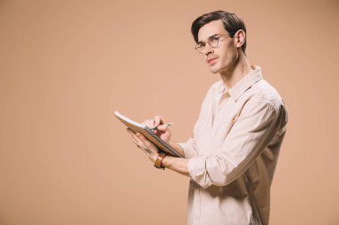 Defter ve bej izole kalem tutan bardaklarda düşünceli adam 