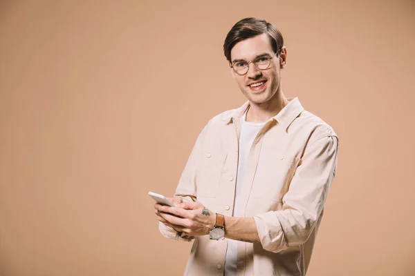 Homem Alegre Óculos Segurando Smartphone Sorrindo Isolado Bege — Fotografia de Stock