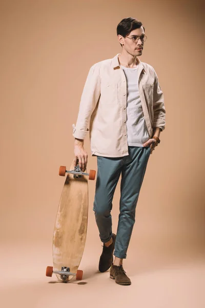 Homem Óculos Segurando Skate Enquanto Com Mão Bolso Isolado Bege — Fotografia de Stock