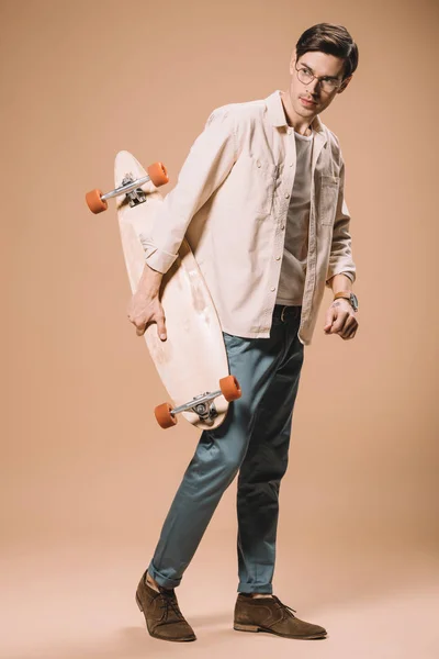 Mann Mit Brille Hält Hölzernes Skateboard Auf Beigem Hintergrund — Stockfoto