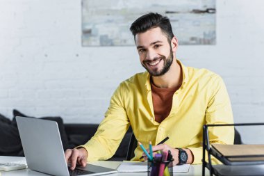 Gülümseyen ve kameraya bakarak, dizüstü bilgisayar kullanarak sakallı işadamı