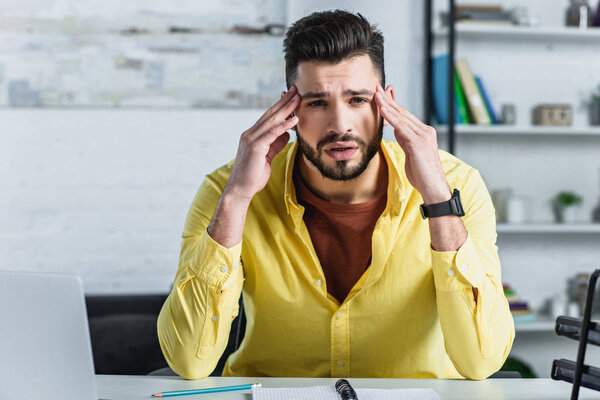 Грустный бизнесмен трогает голову и смотрит в камеру на рабочем месте
