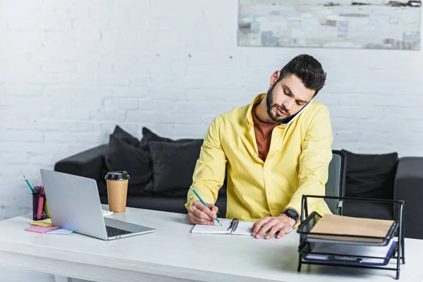 Konzentrierter Bärtiger Geschäftsmann Der Smartphone Spricht Und Notizbuch Schreibt — Stockfoto