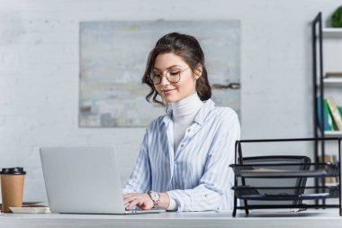 İşyeri dizüstü bilgisayarda yazarak gözlük gülümseyen iş kadını