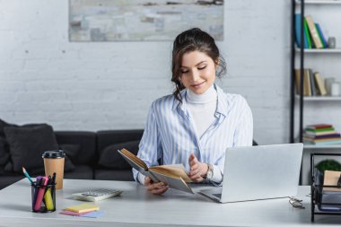 neşeli kadın modern ofis içinde laptop yakınındaki kitap okuma