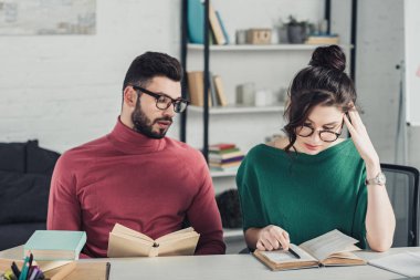 handsome man in glasses looking at female coworker studying with book clipart