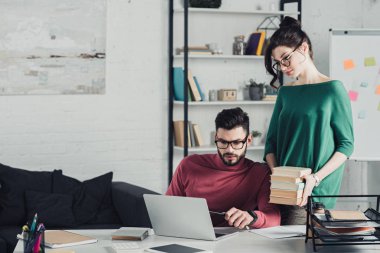 sakallı yakışıklı dizüstü tutan kadın yakınındaki bakarak modern ofiste kitaplar