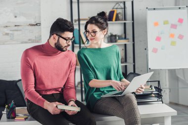 Laptop parmağınızla işaret ve bakarak mutlu neşeli kadın kitap tutan adam sakallı