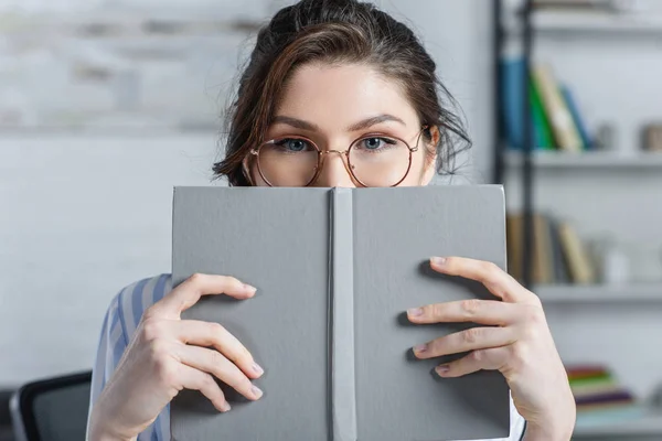Mulher Óculos Cobrindo Rosto Com Livro Escritório Moderno — Fotografia de Stock