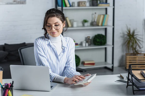 Fröhliche Frau Mit Brille Hält Taschenrechner Neben Laptop Modernem Büro — Stockfoto