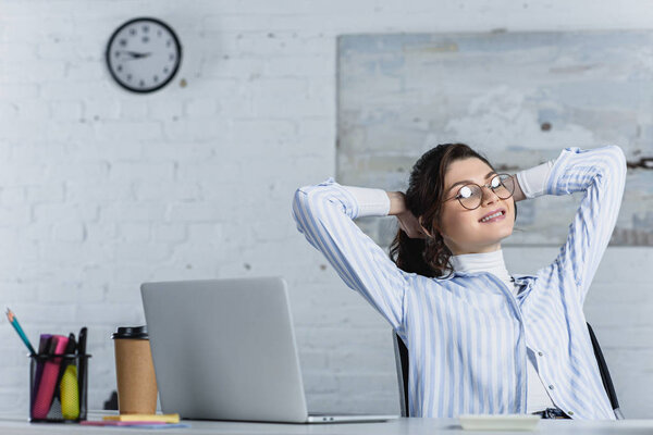 cheerful woman in glasses resting near laptop in modern office 