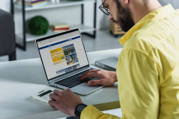 近代的なオフィスに画面上のウェブサイトを予約でノート パソコンに近い電卓を見て髭の男 — ストック写真