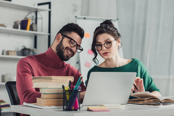 cheerful man in glasses sitting near female colleague in modern office