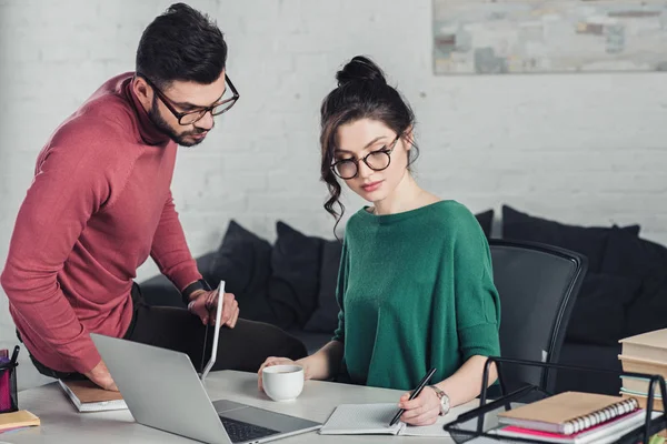 Atractiva Mujer Gafas Escritura Cuaderno Cerca Compañero Trabajo —  Fotos de Stock