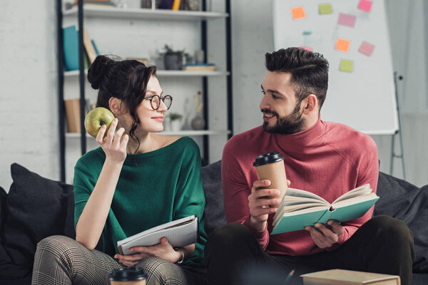 happy woman in glasses looking at bearded man while holding apple in hand