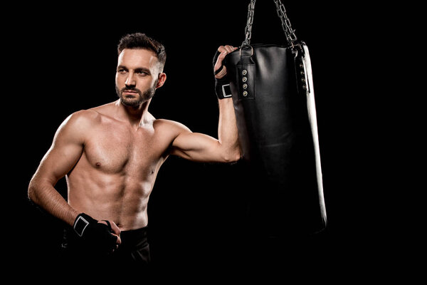 muscular handsome boxer standing near punching bag isolated on black