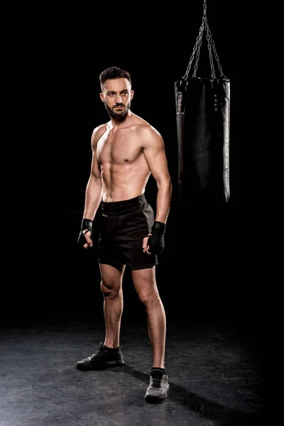 muscular boxer looking at punching bag on black background