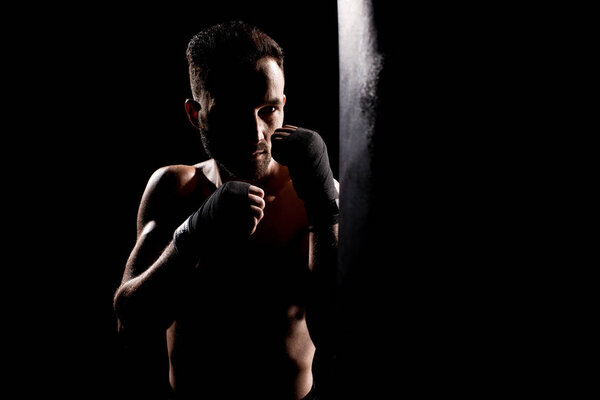 shortless athlete hitting punching bag isolated on black
