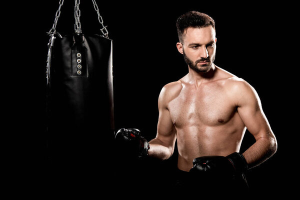 вдумчивый спортсмен в боксёрских перчатках стоит рядом с боксерской грушей, изолированной на черном
