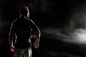 silhouette of football player holding ball on black with smoke  