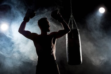 silhouette of muscular athlete in boxing gloves with hands above head on black with smoke clipart