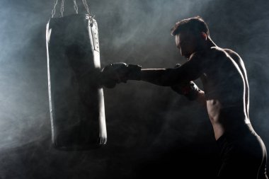 silhouette of athlete in boxing gloves hitting punching bag on black with smoke clipart
