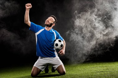 zaferini kutluyor ve siyah duman ile topu tutan neşeli futbol oyuncusu