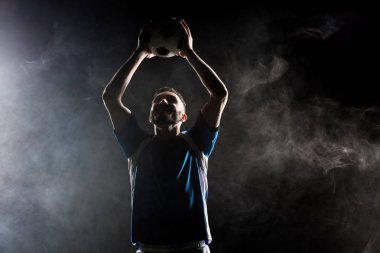 silhouette of handsome football player holding ball above head on black with smoke clipart