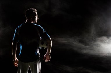 silhouette of football player holding ball on black with smoke   clipart