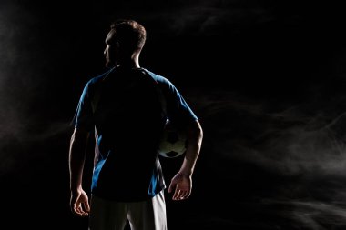 silhouette of football player standing with ball on black with smoke   clipart