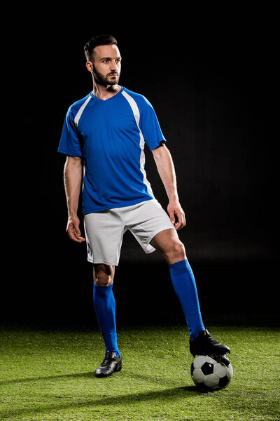 bearded football player standing with ball on grass isolated on black