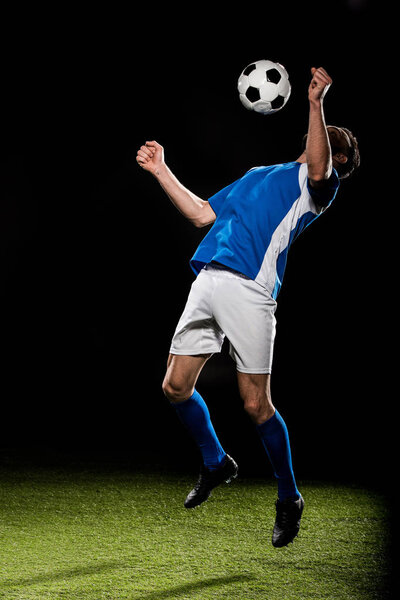 bearded football player in uniform jumping with ball isolated on black