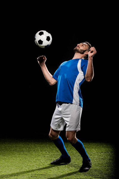 handsome football player in uniform training with ball on grass isolated on black