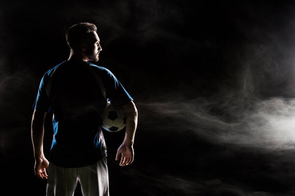 силуэт футболиста, держащего мяч на черном от дыма
  