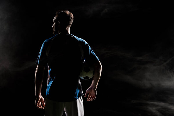 silhouette of football player standing with ball on black with smoke  