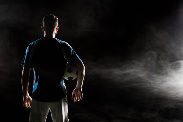 silhouette of man standing in uniform with ball on black with smoke  