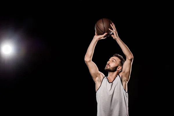 handsome basketball player throwing ball on black background