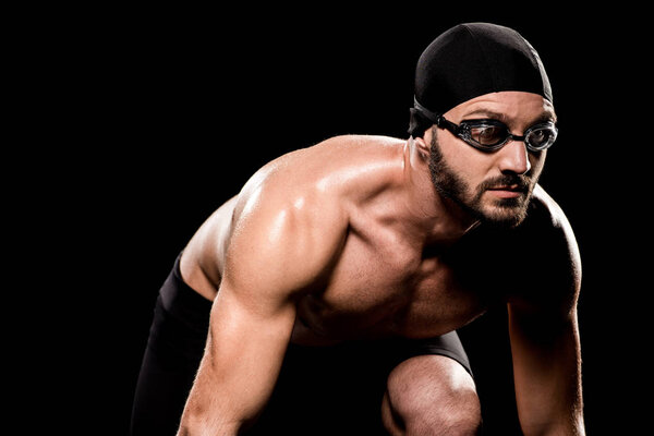 muscular man in goggles standing in start position isolated on black  