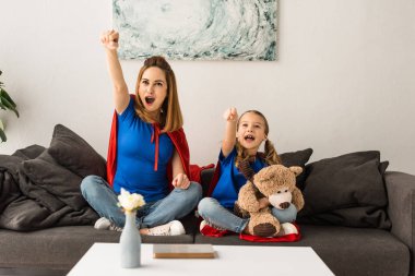 Heyecanlı anne ve kızı koltukta oturan ve evde gülüyor