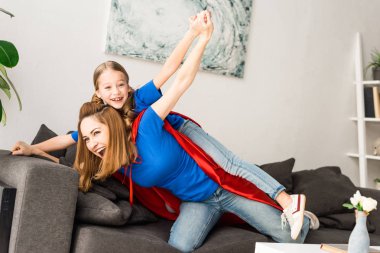 Anne ve kızı evde oynarken kırmızı pelerinler içinde gülümseyen