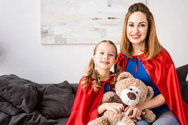 Sonriente Madre Niño Capas Rojas Sosteniendo Oso Peluche Mirando Cámara —  Fotos de Stock