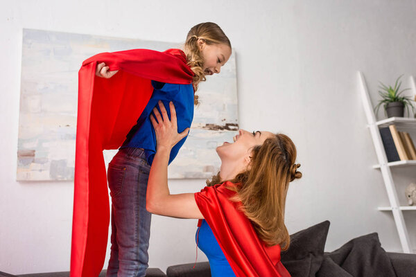 smiling mother and kid in red cloaks playing at home