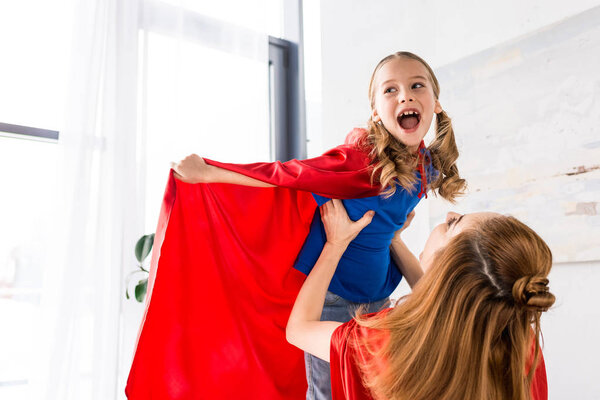 Happy mother and kid in red cloaks playing at home 