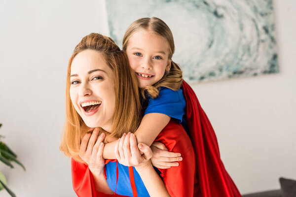 Hugging mother and kid in red cloaks looking at camera 