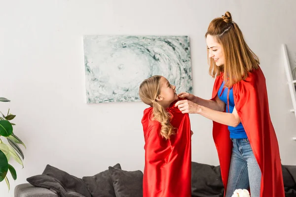 Hermosa Madre Atando Rojo Capa Hija Sonriendo Casa — Foto de Stock